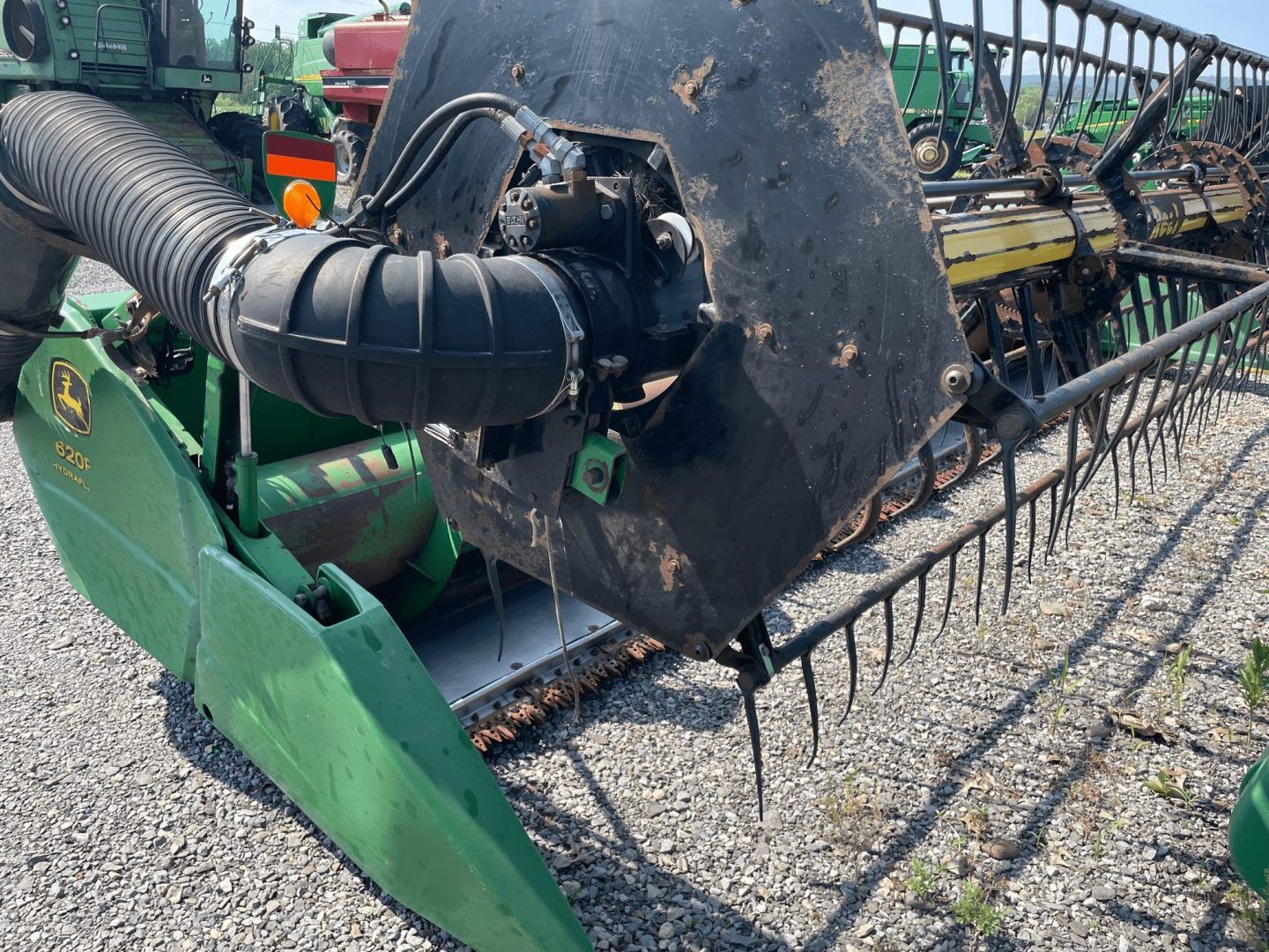 Close-up of a green combine header with black reel and tines on gravel outdoors