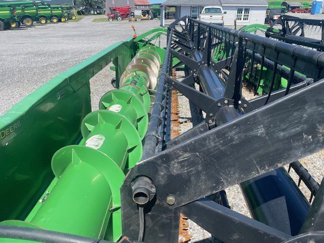 Green agricultural auger beside black machinery in a farm equipment yard