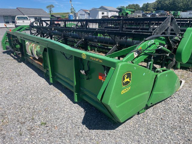 Green John Deere combine header parked outdoors on a gravel lot