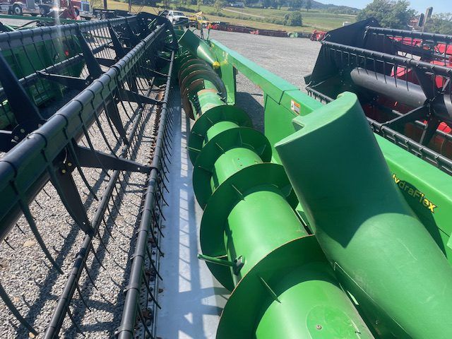 Close-up of a green combine harvester header with metal augers in a farm field outdoors
