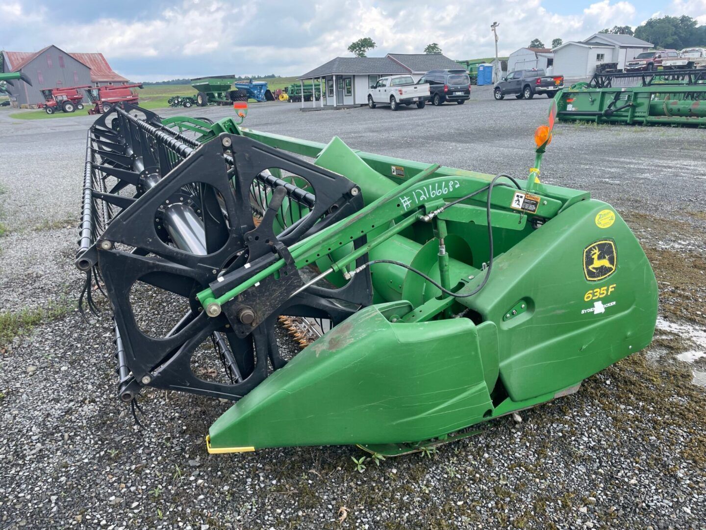 Green farm tractor attachment with black front loader on gravel in an outdoor lot