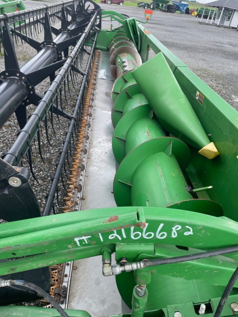 Green agricultural machine with large auger beside black conveyor in a grain-filled facility