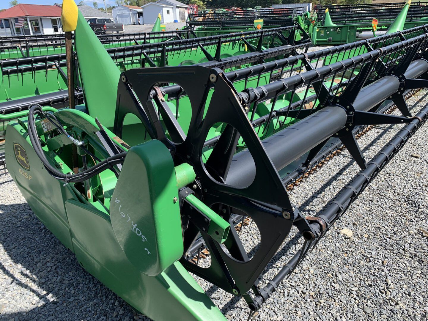 Green combine harvester header with black reel, parked outdoors on gravel.