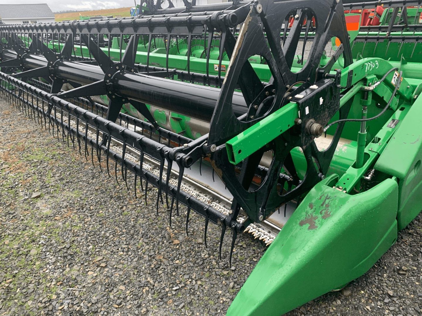 Green combine harvester header with cutting reel and tines on a gravel lot
