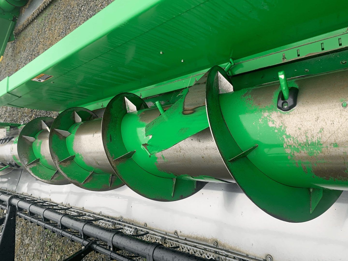 Green auger conveyor blades inside a metal trough, viewed from the side.