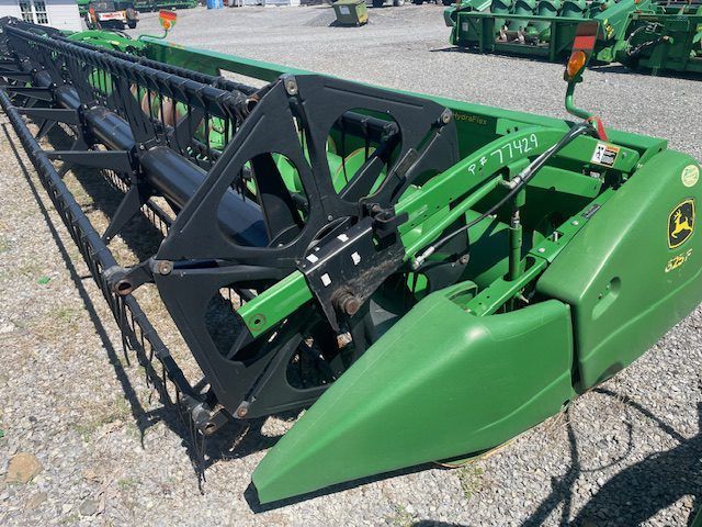 Green and black John Deere combine header on gravel lot