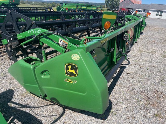 Green John Deere farm implement parked on gravel lot, side view