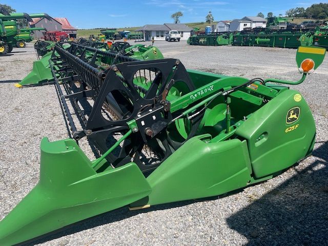Green John Deere combine header parked on gravel lot, with black reel and cutter bar.