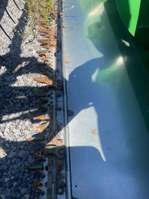Close-up of a train wheel and rail track beside gravel, with a green railcar casting shadows