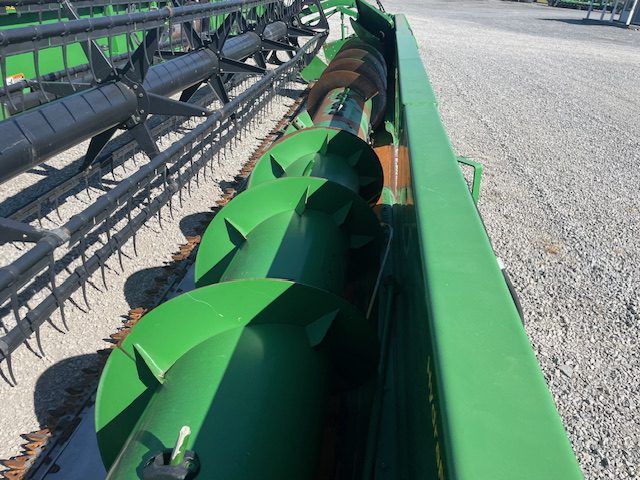 Green combine harvester header cutting crops in a field, viewed close up from above