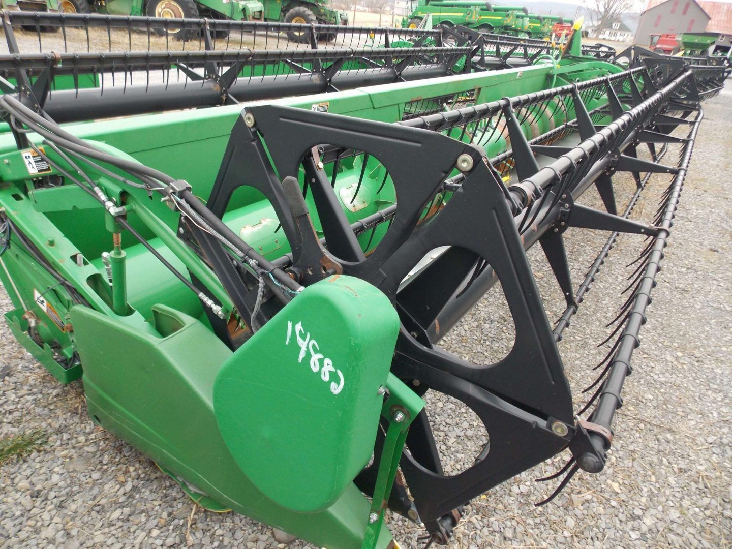 Green agricultural combine header with black cutting reel parked on gravel outdoors