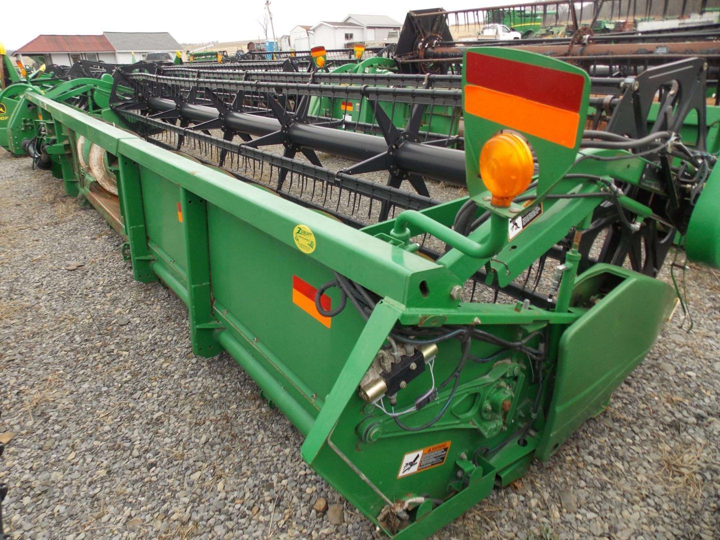 Green agricultural harvesting machine with orange hazard lights on a gravel lot