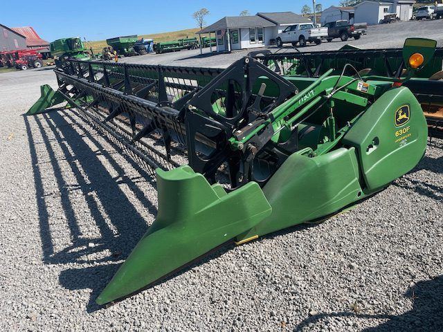 Green agricultural combine header parked on gravel lot, with black reel and cutting bar.