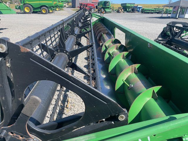 Close-up of a green combine harvester header with auger and black frame in a farm equipment yard