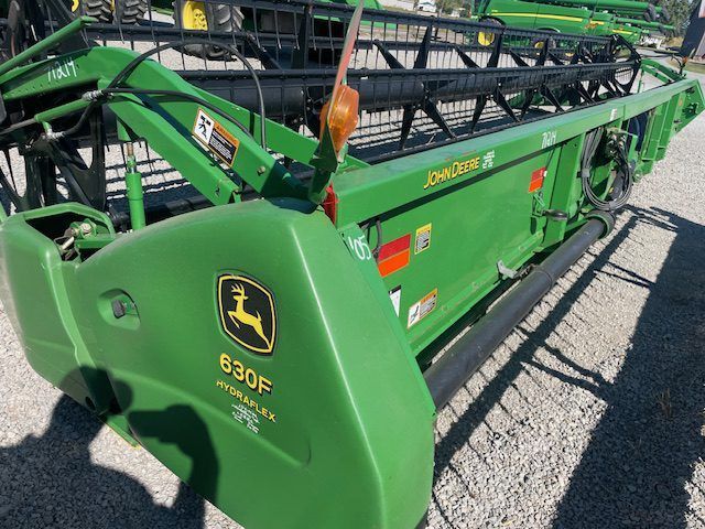 Green John Deere 630P combine header parked outdoors on gravel, side view