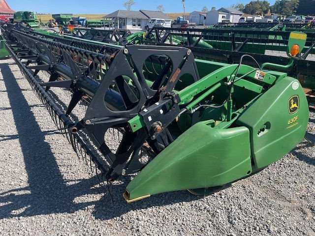 Row of green and black agricultural headers parked on gravel outdoors