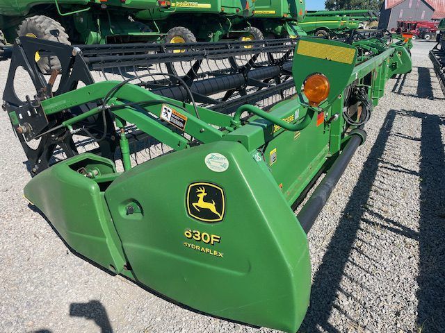 Green John Deere 630F combine header parked outdoors on gravel.