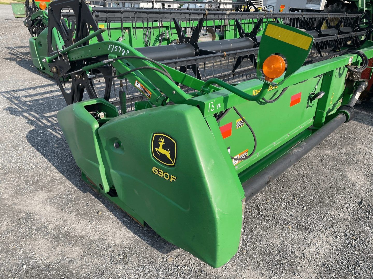 Green John Deere farm machine parked on gravel lot, with yellow logo and black header attachment