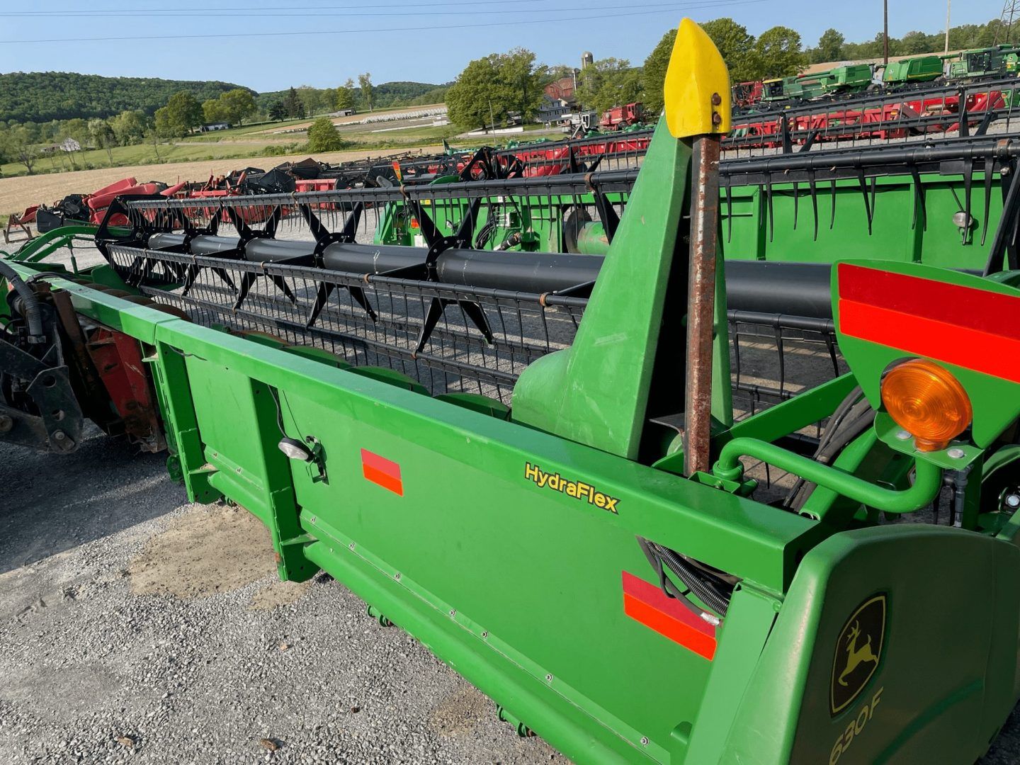 Green agricultural combine header parked on gravel, with black cutting reel and yellow end cap.