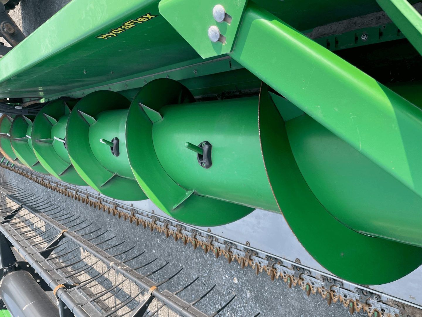 Close-up of green auger blades on a farm machine above a conveyor belt