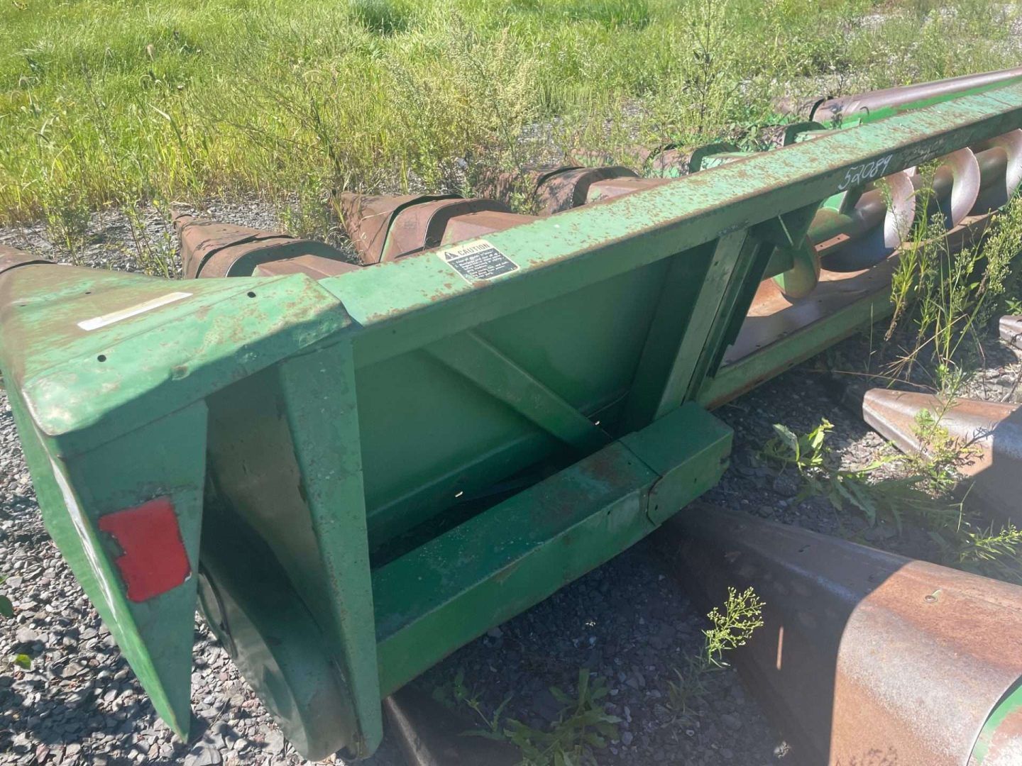 Green industrial trailer or machinery frame lying on its side outdoors in grass and dirt.