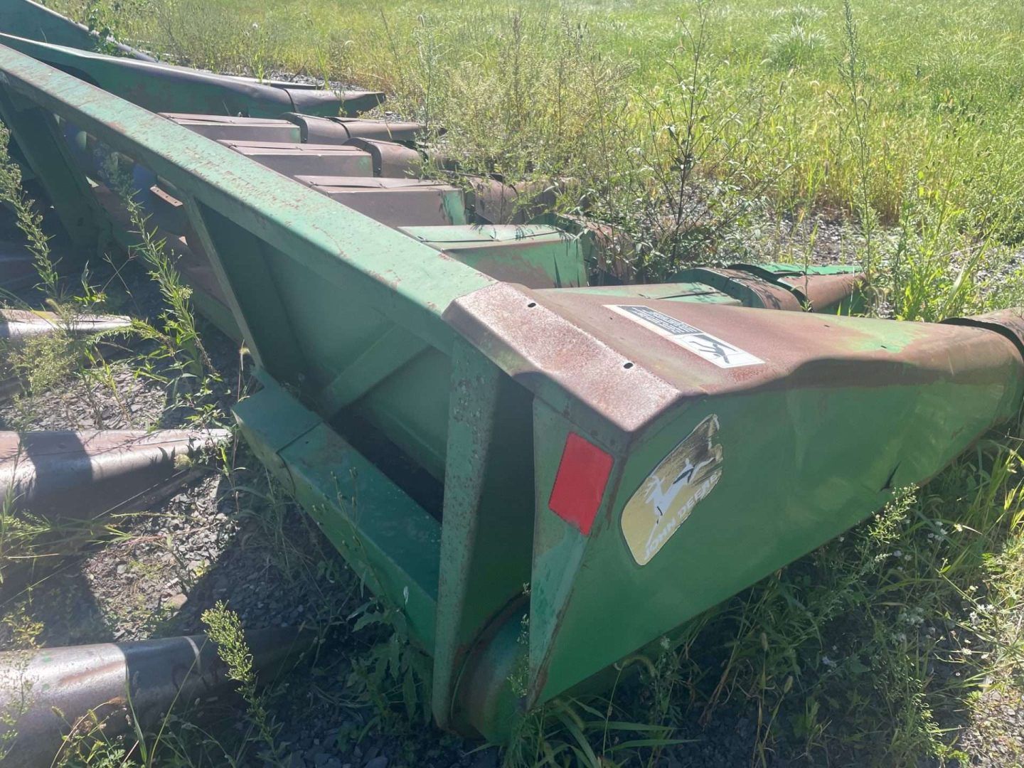 Green metal farm trailer tipped on its side in a grassy field, with a bent front corner and red reflector.