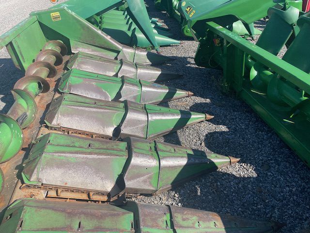 Rows of green agricultural cutting heads with worn metal blades on gravel.