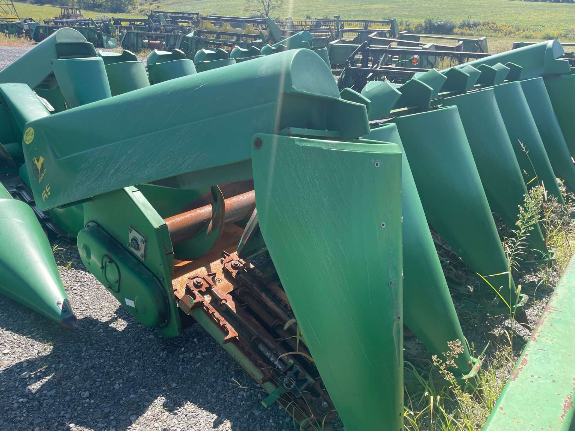 Rows of green metal farm machinery parts stacked outdoors in a field or yard
