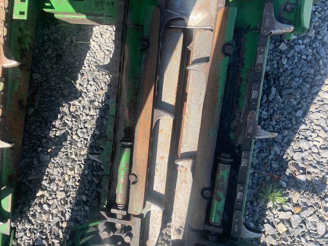 Close-up of a green and beige machine part amid gravel and metal rails.
