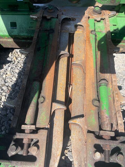 Rusty coupler and hydraulic hoses on green farm machinery, viewed from above.
