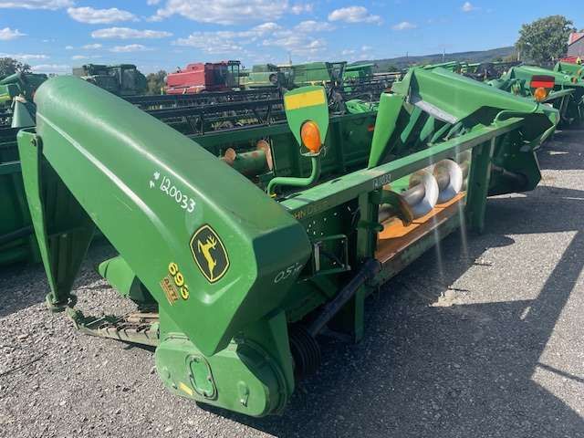 Green John Deere rotary mower attachment parked outdoors on pavement under a sunny sky