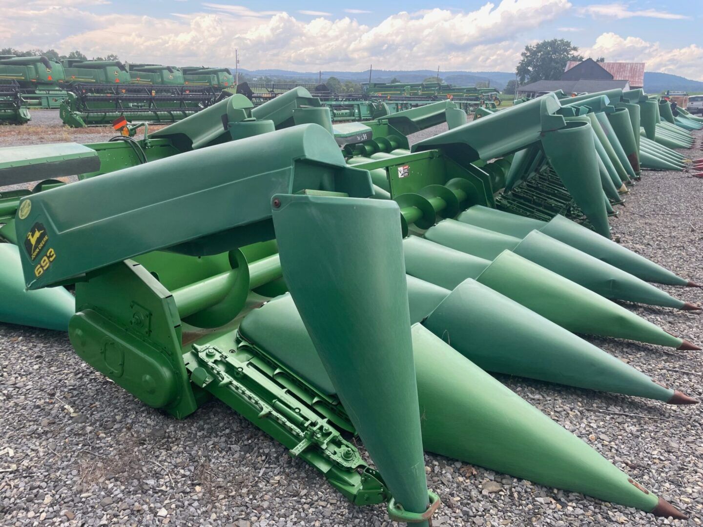 Rows of green farm combine corn headers with pointed snouts in an outdoor yard.