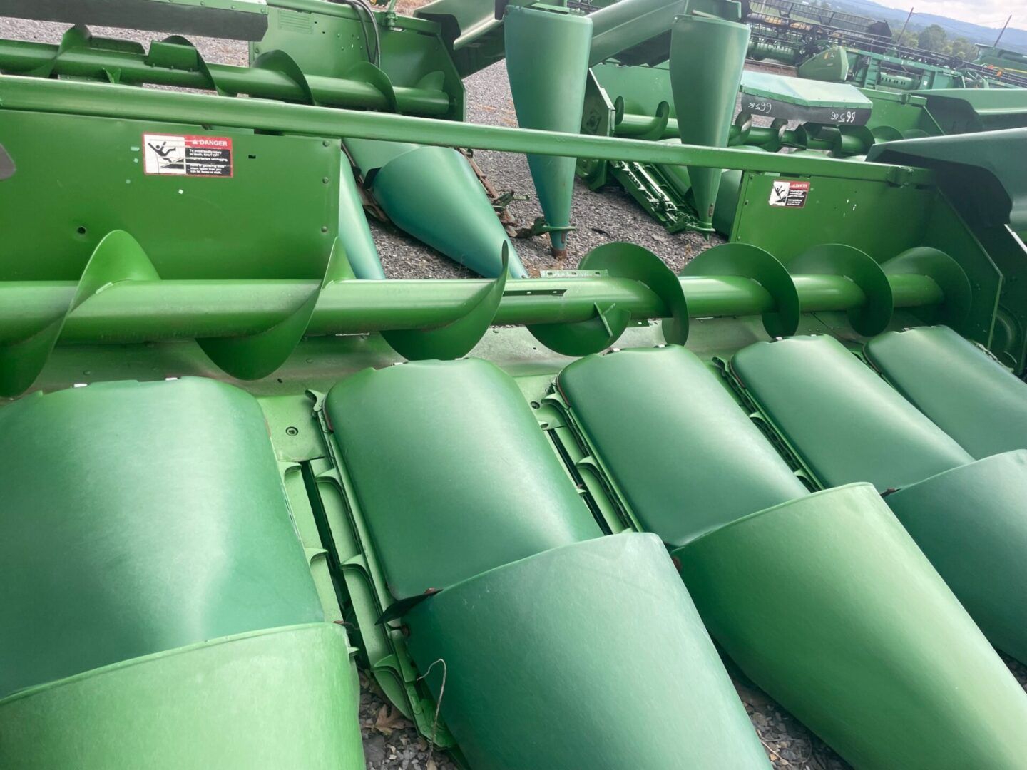 Green agricultural machine with metal harvesting blades and conveyor parts in a field.