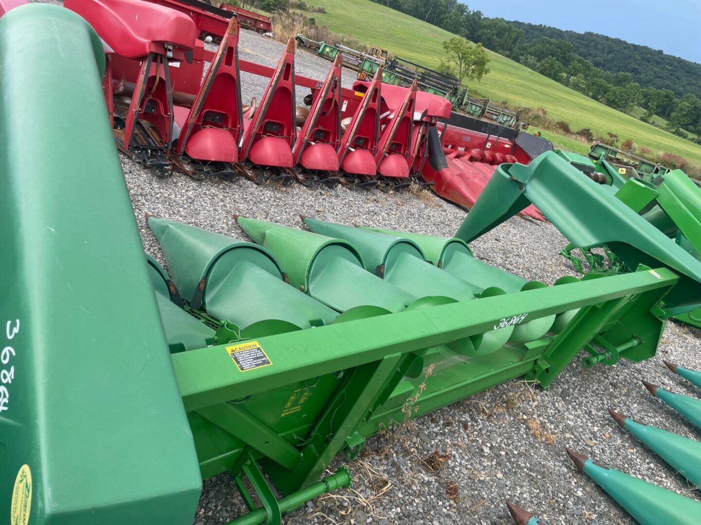 Green and red farm harvesters lined up on gravel in a rural field setting
