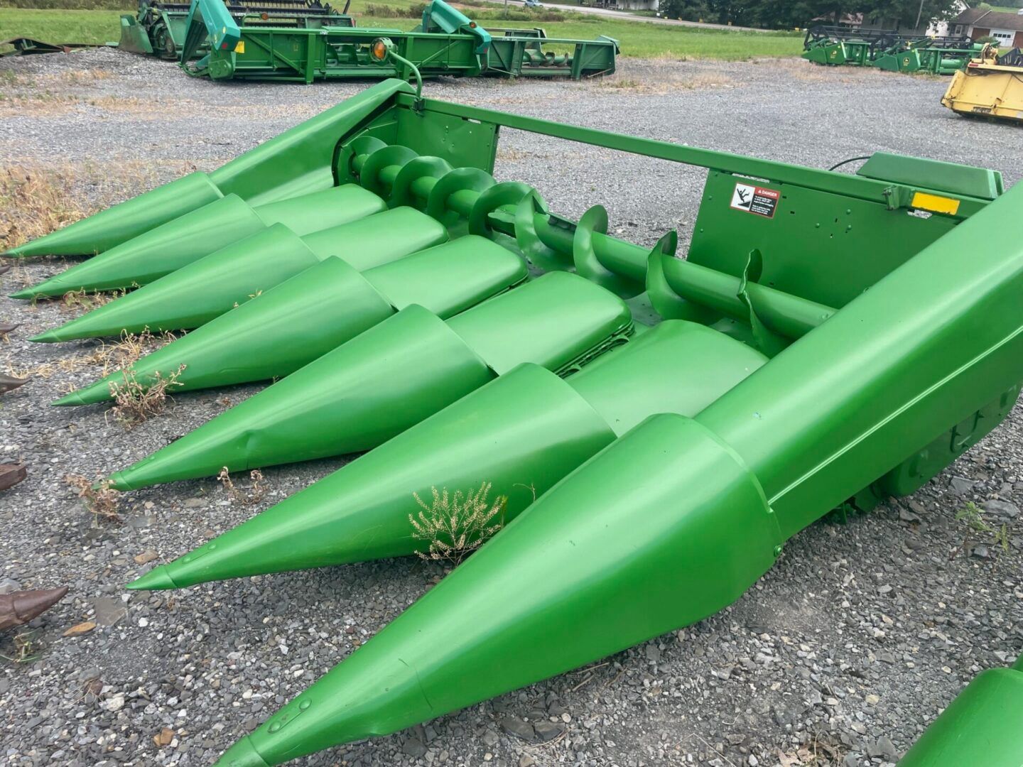 Green corn header with pointed cones on a farm implement, shown on gravel outdoors