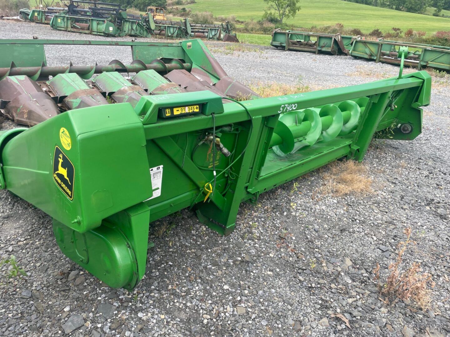 Green agricultural mower attachment on gravel in an outdoor farm equipment yard