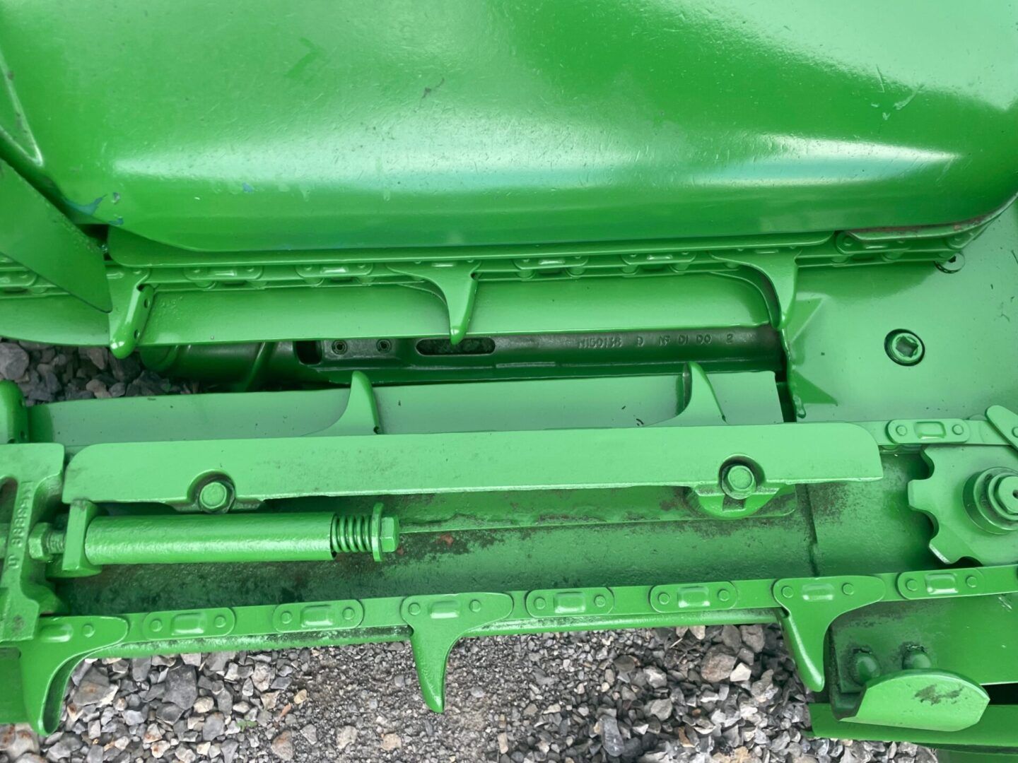 Close-up of green agricultural machinery with hydraulic cylinder and metal frame over gravel.