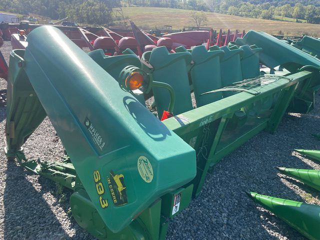Green farm equipment parked on gravel, with rows of red machinery and fields in the background
