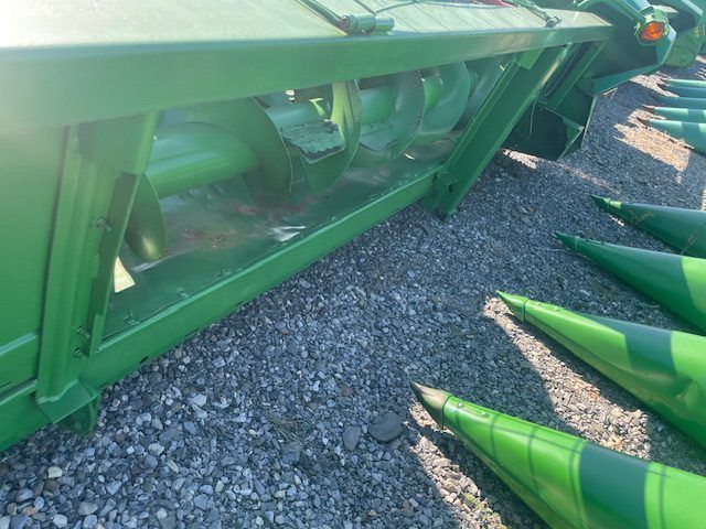 Green industrial machine parts on gravel, with pointed metal cones stacked nearby.