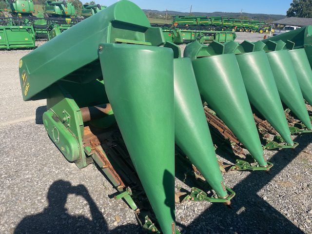 Green corn header with pointed metal cones lined up in a farm equipment lot