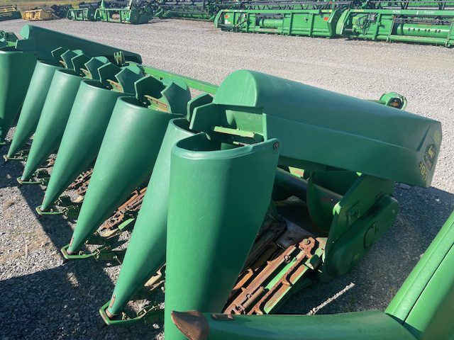 Green farm implement with multiple pointed cones and metal frame on gravel lot