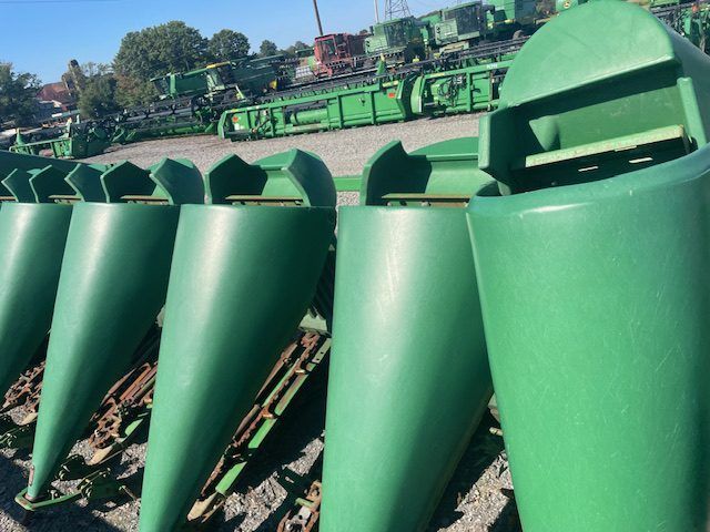 Green agricultural harvesting machinery lined up outdoors in a field under clear daylight