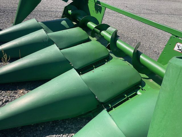 Green agricultural harvesting machine with rotating drum and metal tines on pavement