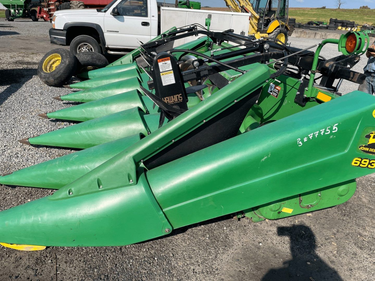 Green agricultural mower attachments lined up in a gravel lot beside a white truck