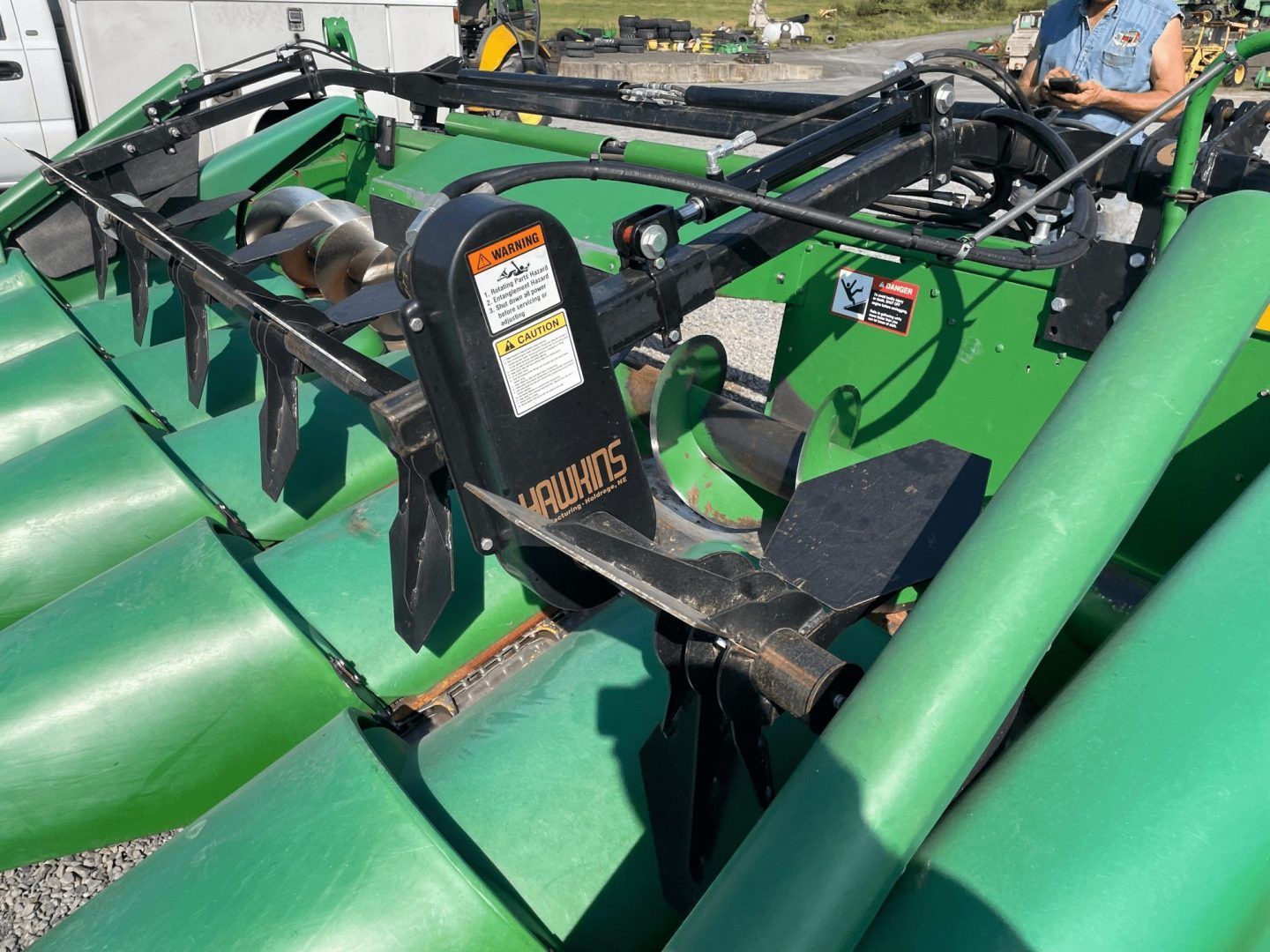 Green agricultural machine with black metal arms and a tractor cab in the background