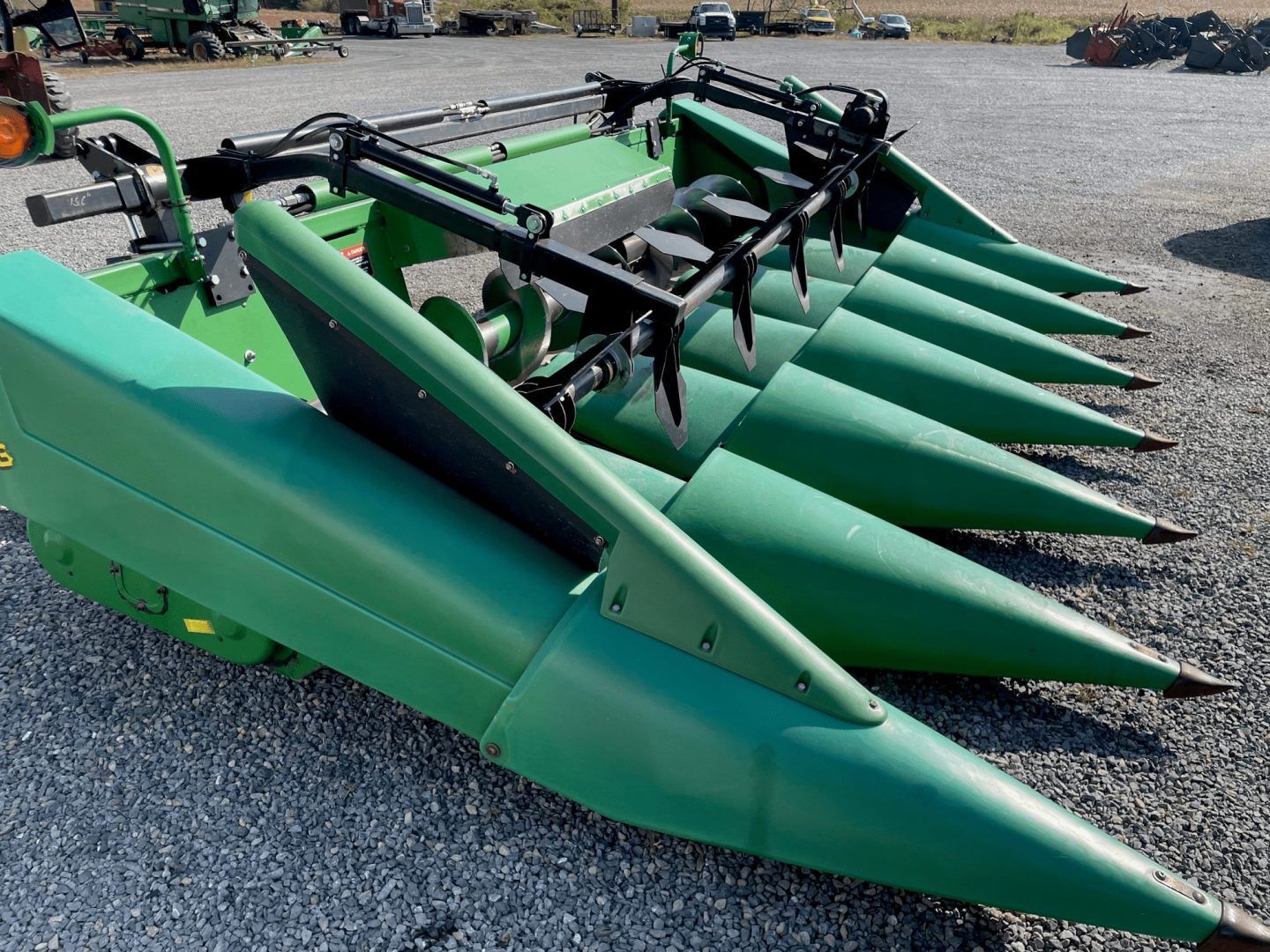 Green corn harvester header with multiple pointed metal cutting rows on gravel
