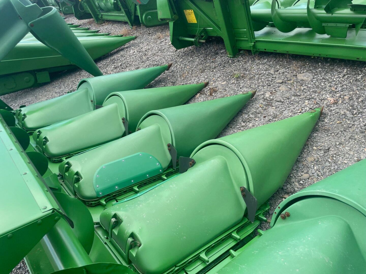 Green agricultural machine parts with cone-shaped rollers on gravel outdoors