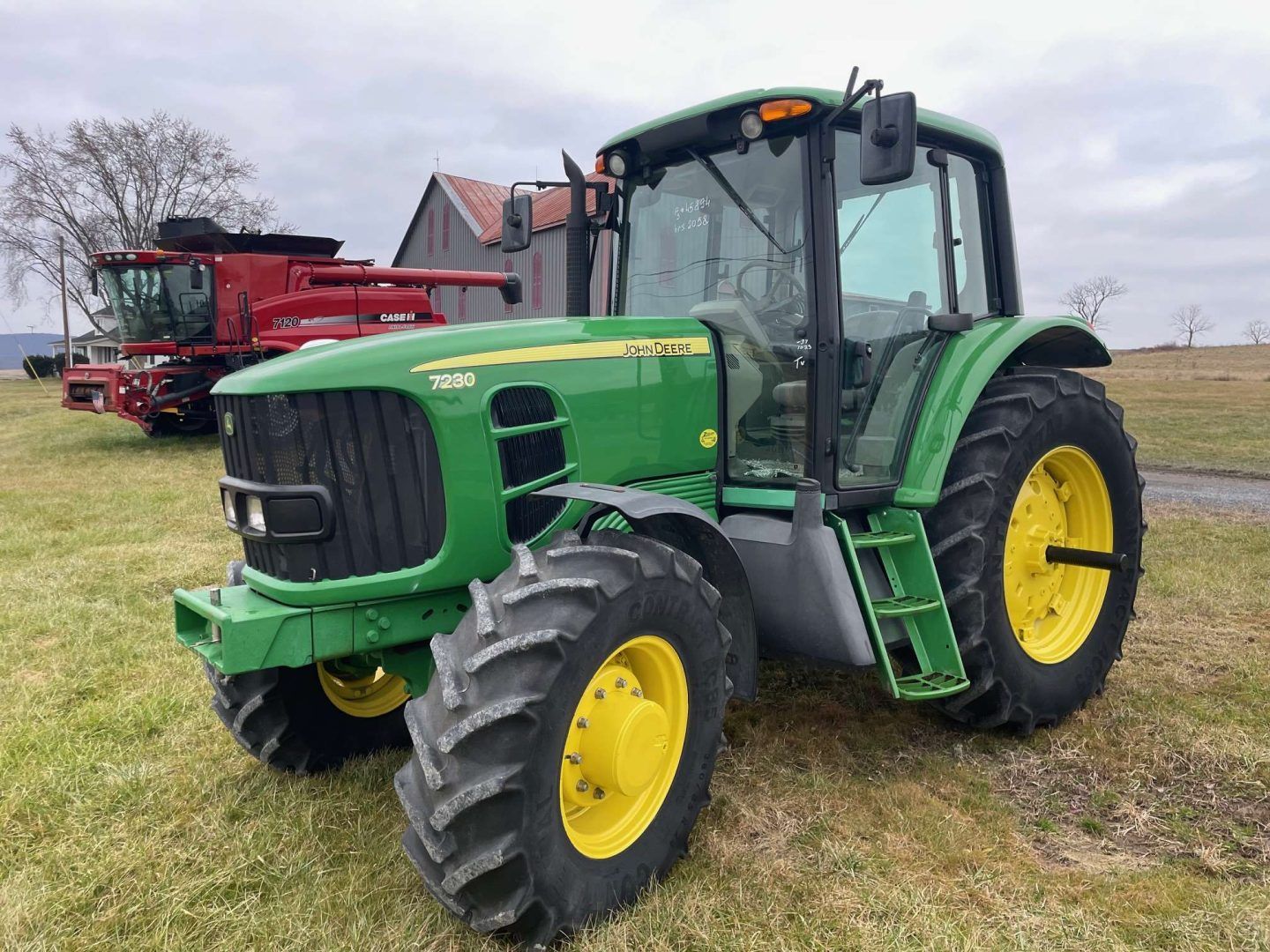 Green John Deere tractor with yellow wheels parked in a field, with farm equipment in the background
