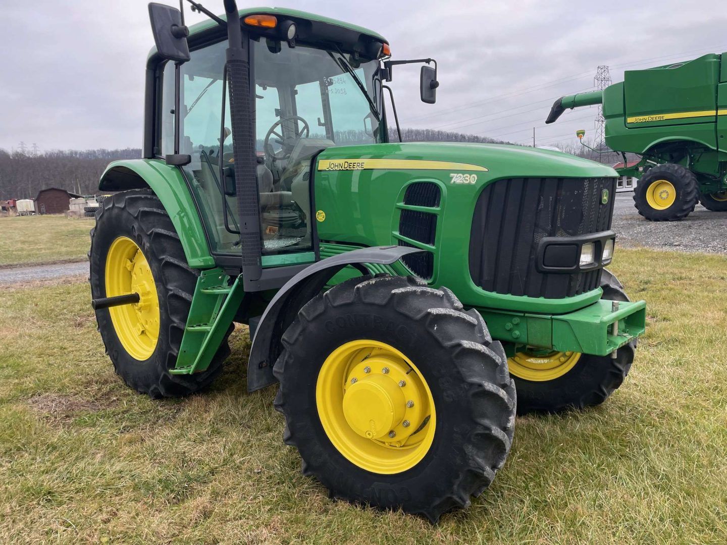 Green John Deere tractor with yellow wheels parked on a farm lot under a cloudy sky