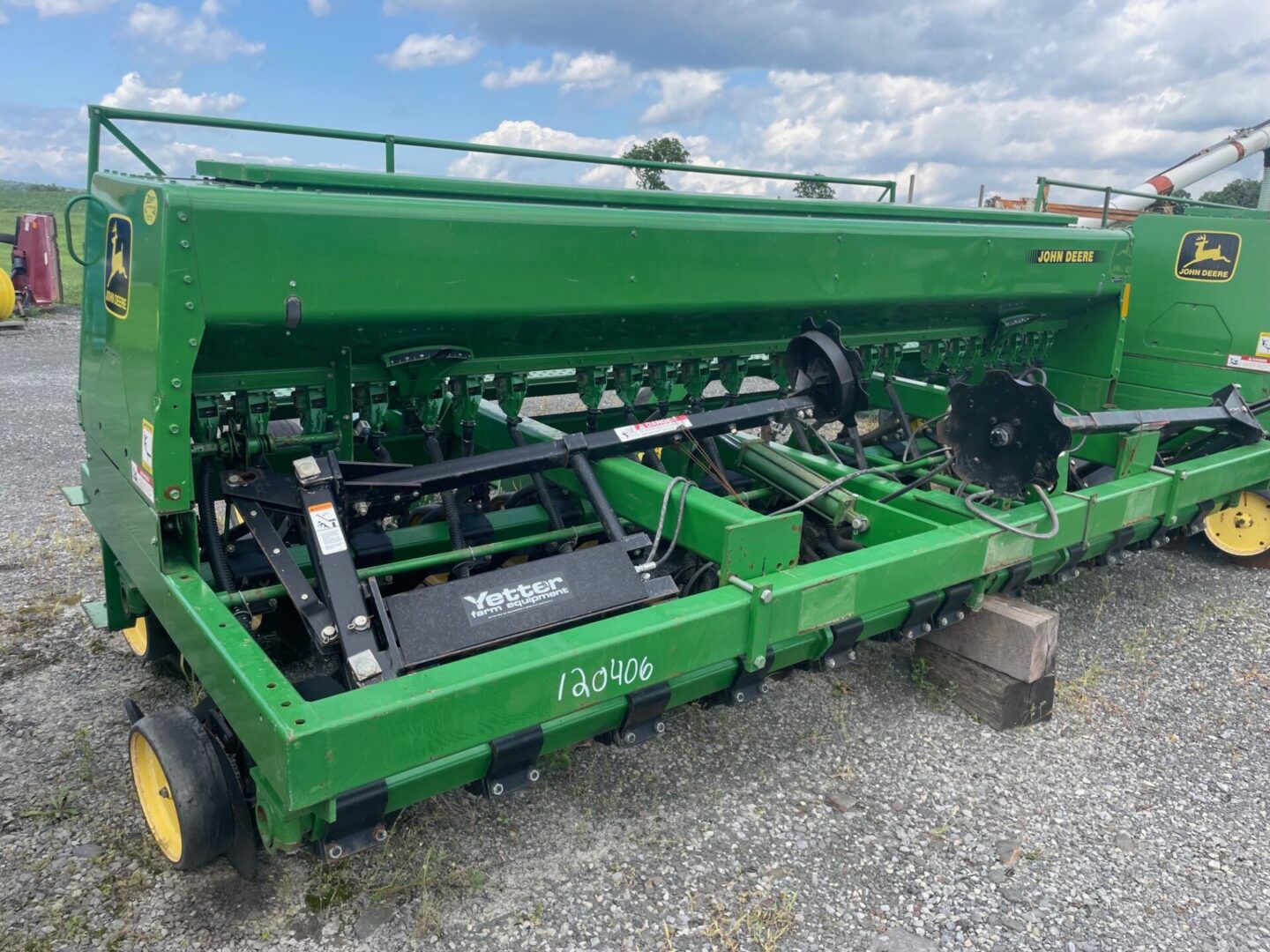 Green agricultural machine on gravel lot, with open front showing internal механизмs under a cloudy sky